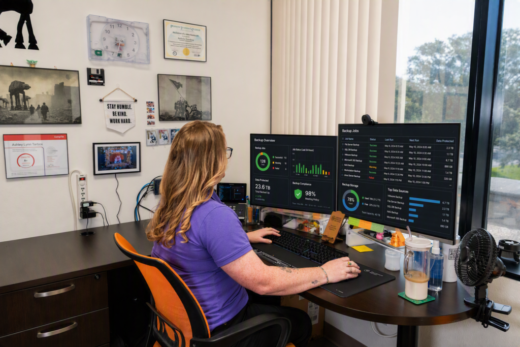 Backup Dashboard Monitoring and Managed IT Support Managed IT services technician monitoring backup dashboards and data protection status across multiple computer monitors in a modern office.