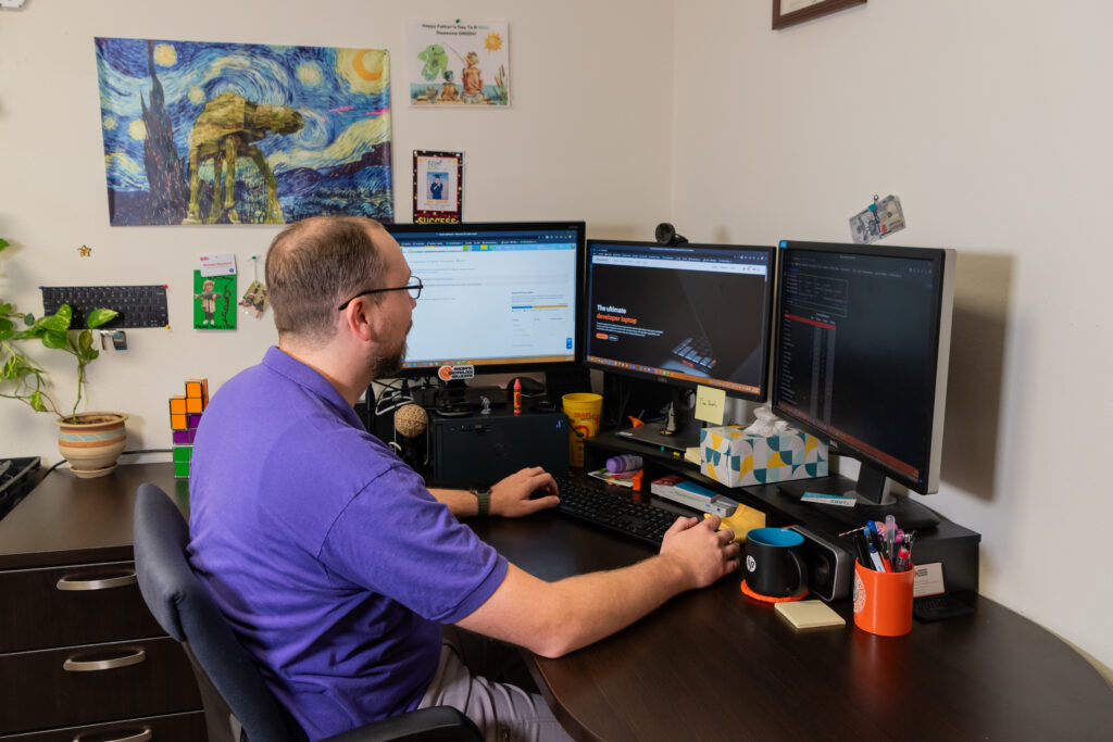 Radiant Technology Solutions technician working at a multi-monitor workstation providing remote IT support, cybersecurity monitoring, and managed IT services for business clients.